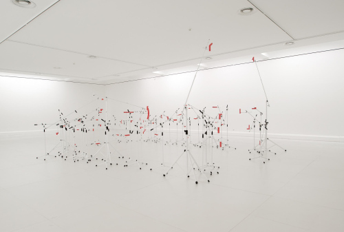 History in the MakingRauminstallationLackierte Mikrofonständer, pulverbeschichtete Metallelemente, RohrschellenEngländerbau Vaduz, Kunstraum Liechtenstein2013Pressetext:Alexandra Berlinger und Wolfgang Fiel sind unter dem Namen tat ort in den Bereichen Bildende Kunst, Architektur und Urbanismus tätig. Nach über einer Dekade des gemeinsamen Arbeitens haben sie nun für den Kunstraum Engländerbau unter dem Titel History in the Making eine Rauminstallation entwickelt, die sie als retroaktives Manifest ihrer künstlerischen Praxis verstehen. Ein häufig wiederkehrendes Motiv ist dabei ihre Auseinandersetzung mit der temporären Formation kollektiver Prozesse und den dabei ausgetragenen Konflikten. In vielen Fällen bleibt die Arbeit des Künstlerduos auf die Zeit beschränkt, die sie vor Ort verbringen und dort oft mehrere Wochen in einen gegebenen Kontext eintauchen. Dass selbst die Konstitution des physischen Raums davon nicht unberührt bleibt, zeigt sich nicht zuletzt an den temporären ‚Apparaturen‘, die Berlinger und Fiel für ihre Interventionen konstruieren.&nbsp;Sie beschäftigen sich dabei unter anderem mit der Frage, inwieweit diese Strukturen potentiell auf unsichtbare/verborgene Prozesse verweisen können und dabei zwischen eigenständiger Form und funktionalem Hilfsmittel changieren. Im Gegensatz zu den unterschiedlichsten Objekten und Materialien die in ihren Arbeiten zum Einsatz kommen, verstehen sie die geschaffenen Environments als Katalysatoren von Prozessen, die im Idealfall den Zeitraum der ursprünglichen Inszenierung überdauern.&nbsp;Wichtiger Bestandteil ihrer Werkdokumentation ist die minutiöse digitale Archivierung der eingesetzten Mittel, die ihnen erlaubt, die eigene Entwicklung retrospektiv als vielschichtige Sequenz diskreter Ereignisse zu begreifen, deren ‚Spuren‘ einen Namen tragen, denen sie die Treue halten.&nbsp;Die digitalen Ressourcen ausgewählter Arbeiten werden für die Ausstellung zu einer imaginären Großform innerhalb der räumlichen Begrenzungen des Engländerbaus assembliert, die aber lediglich mittelbar angezeigt, vorgebracht, eingefasst oder abgetastet wird. Die zu diesem Zweck verwendeten handelsüblichen Mikrofonstative sind die justierbaren Träger eines jeweils an deren Ausleger montierten Passstücks, das der Kontur der imaginären Skulptur an einer bestimmten Stelle nachgeformt ist, und sich somit in ihrer Gesamtheit zu einem räumlichen Ensemble verdichten. Die Installation ist die physische Manifestation einer historischen Fiktion.&nbsp;Die zur Ausstellung erscheinende Publikation dokumentiert die digitalen Ressourcen der ausgewählten Projekte und liefert somit den Bauplan zur räumlichen Inszenierung.Fotos Barbara Bühler, ©tat ort(tat ort)